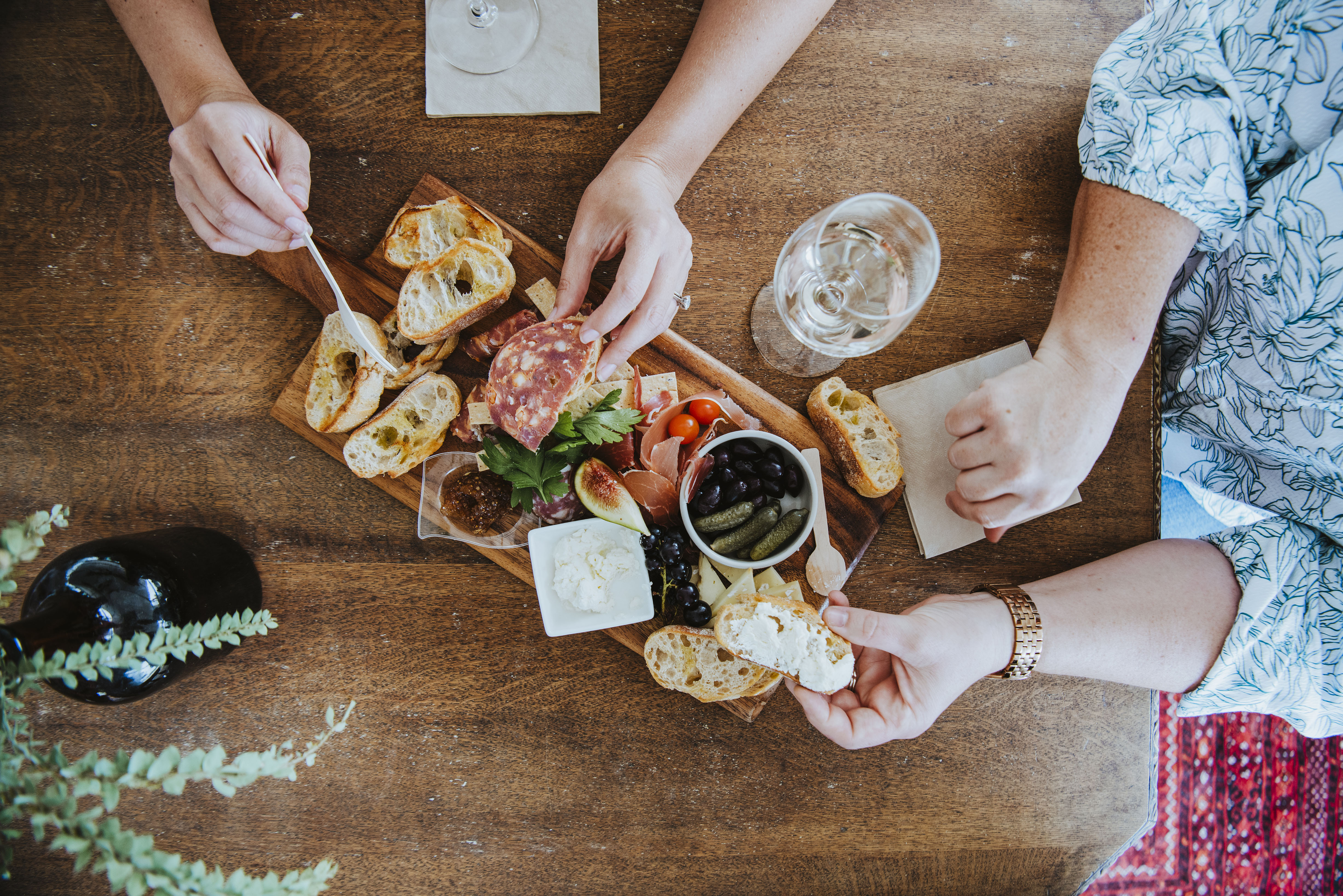 Charcuterie platter on table with 2 people's hands and arms 